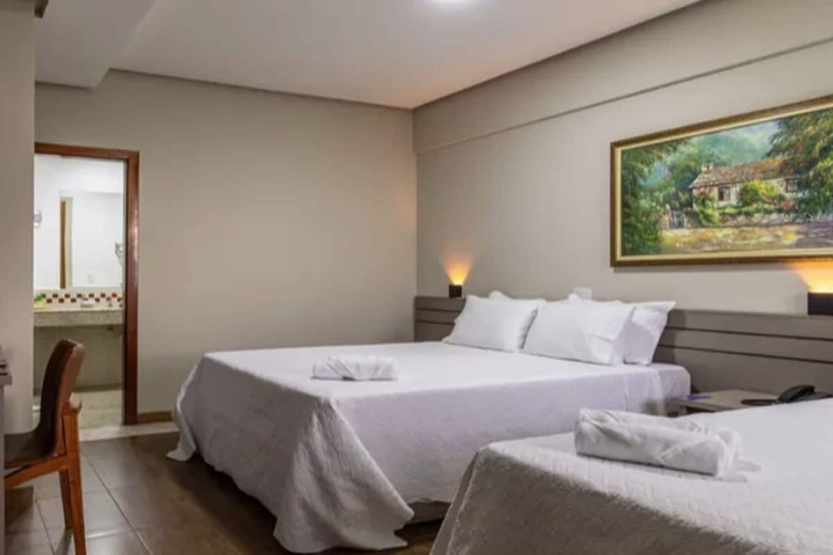 Hotelkamer met twee bedden, een bureau, een stoel, een schilderij aan de muur en uitzicht op een huis door het raam.