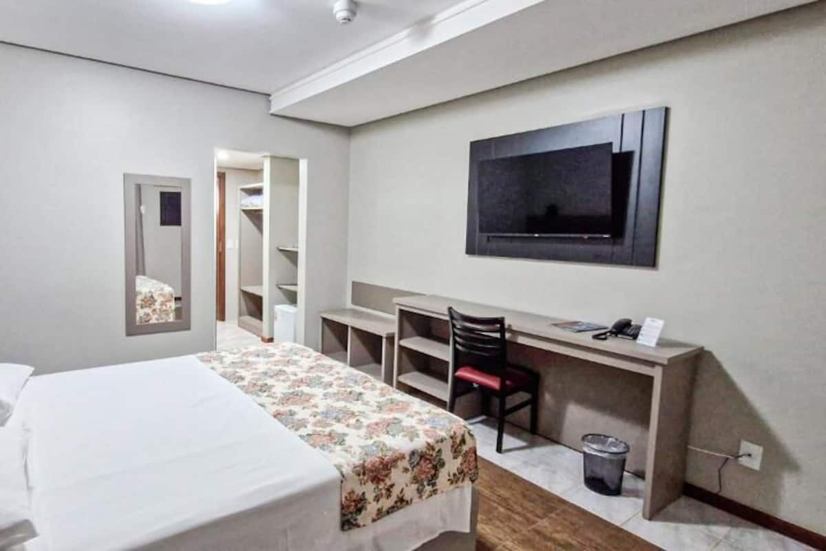 Een hotelkamer met een bed, een bureau, een stoel, een televisie en een kledingkast.