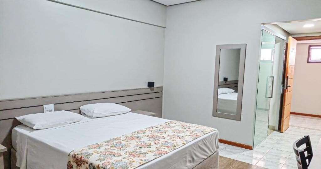 A hotel room with a bed, a bedside table, a mirror, and a door leading to a bathroom.