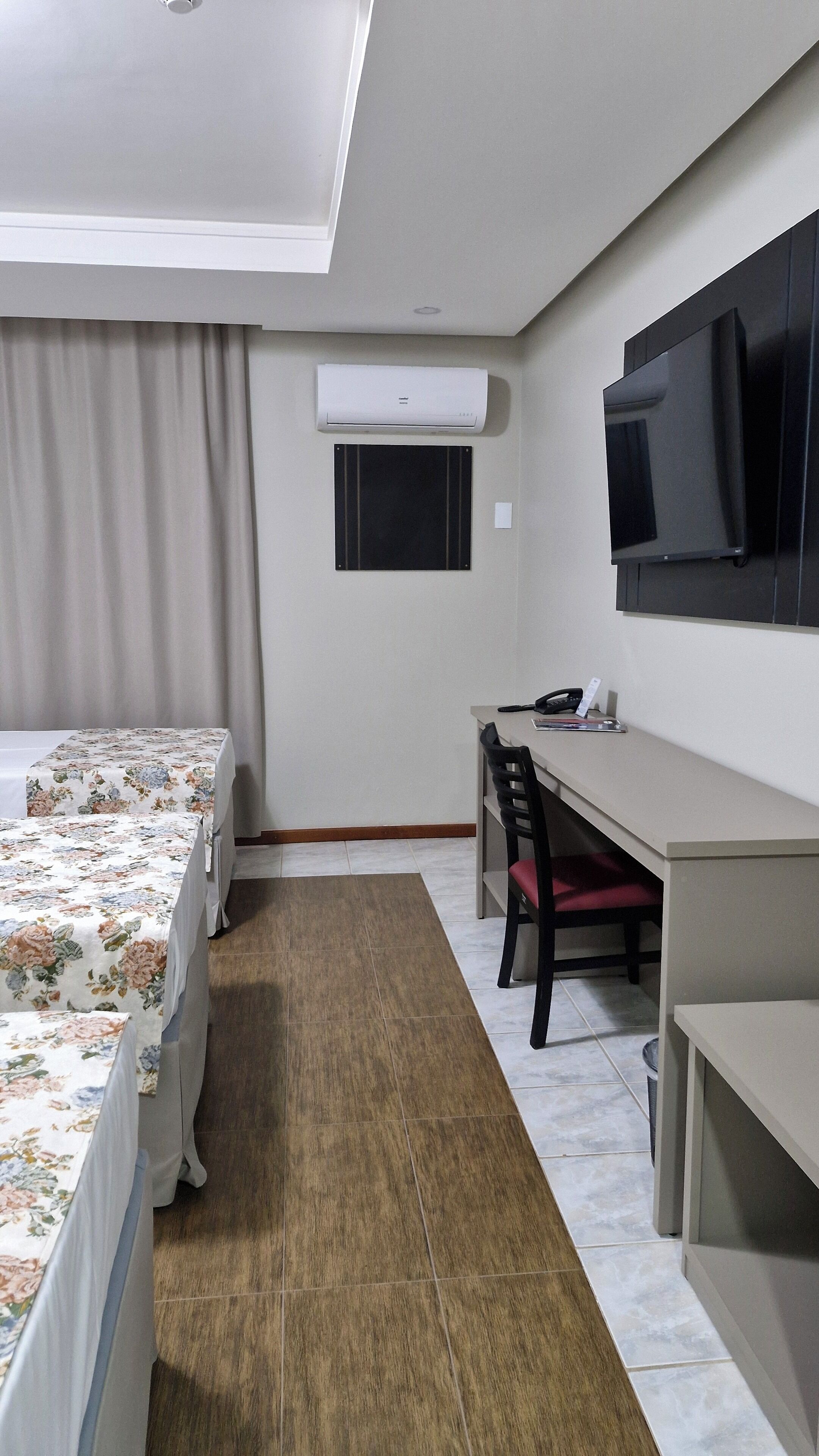 Habitación de hotel con cama, escritorio, silla, televisor y aire acondicionado.