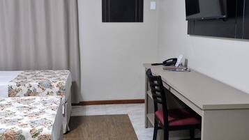 Quarto de hotel com cama, escrivaninha, cadeira, televisão e ar condicionado.