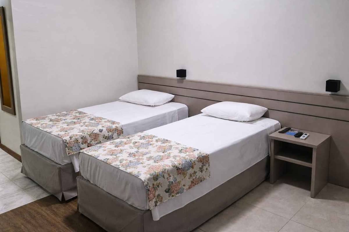 Een hotelkamer met twee enkele bedden, een nachtkastje en een wandlamp.