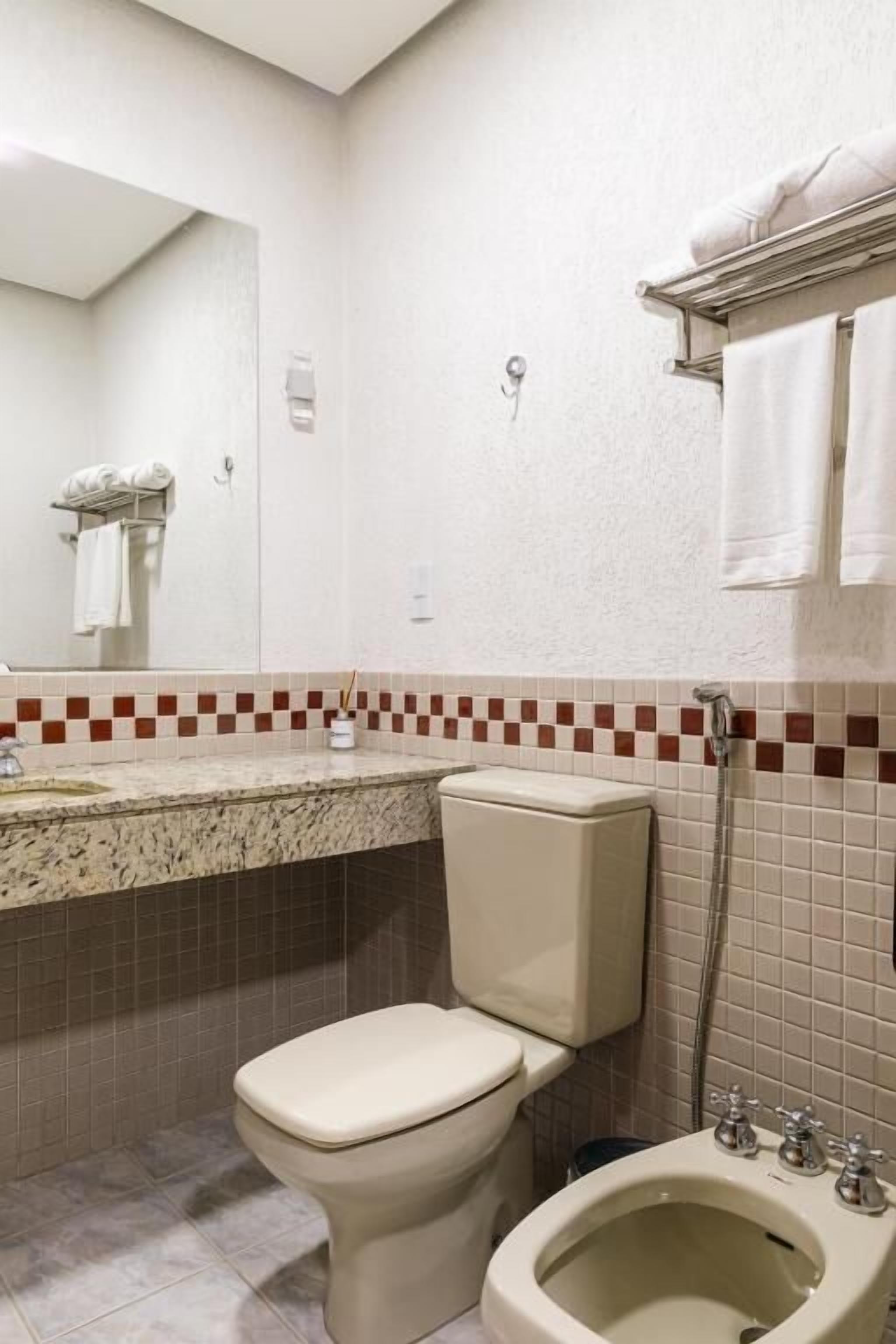 Un baño con inodoro, bidé, espejo y toallero.