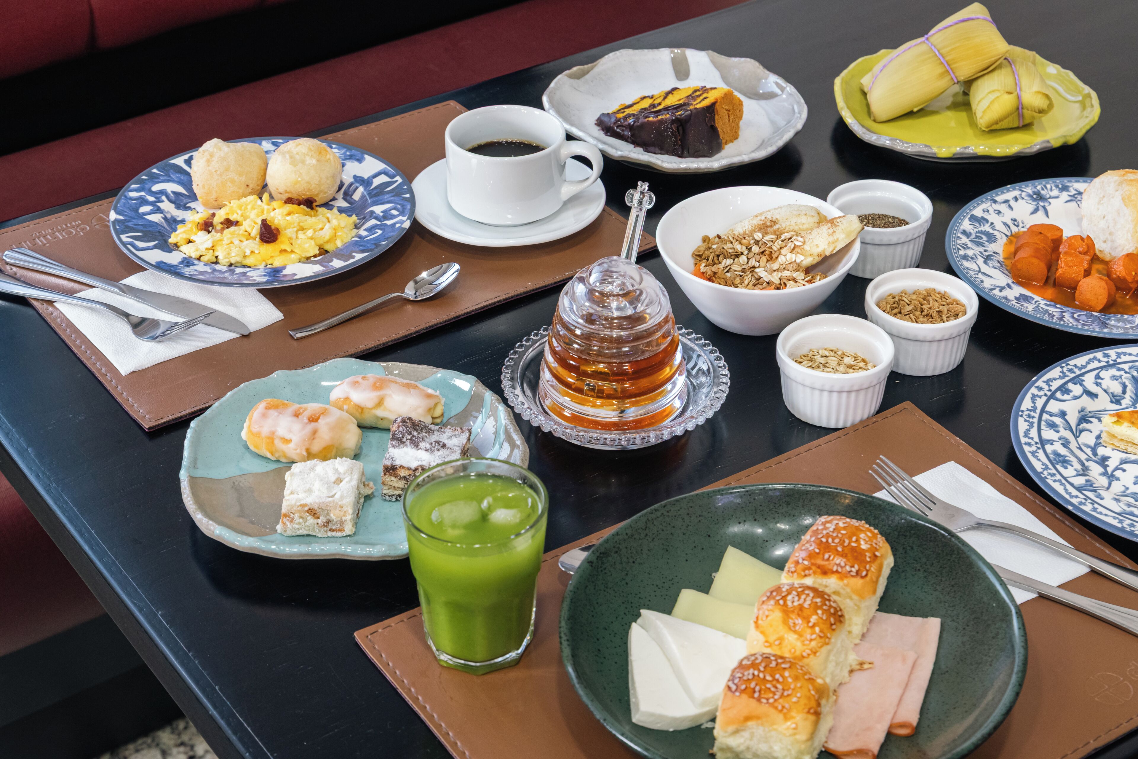 A table set with various breakfast items including pastries, a glass of green juice, and a plate of cheese and ham.
