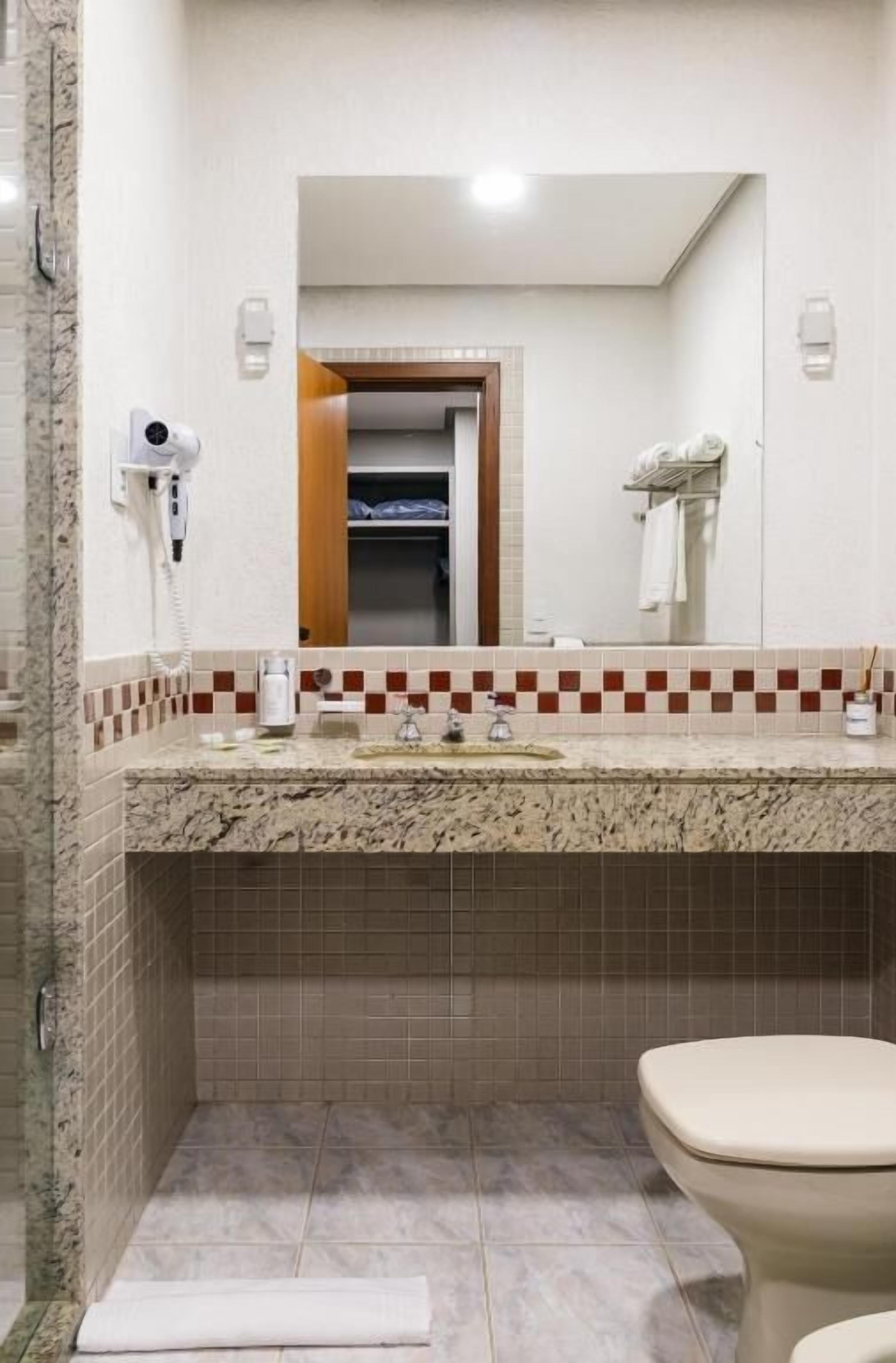 A bathroom with a marble countertop, a mirror, a towel rack, and a shower area.