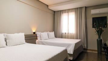 A hotel room with two beds, a nightstand, a vase with flowers, and a window with curtains.