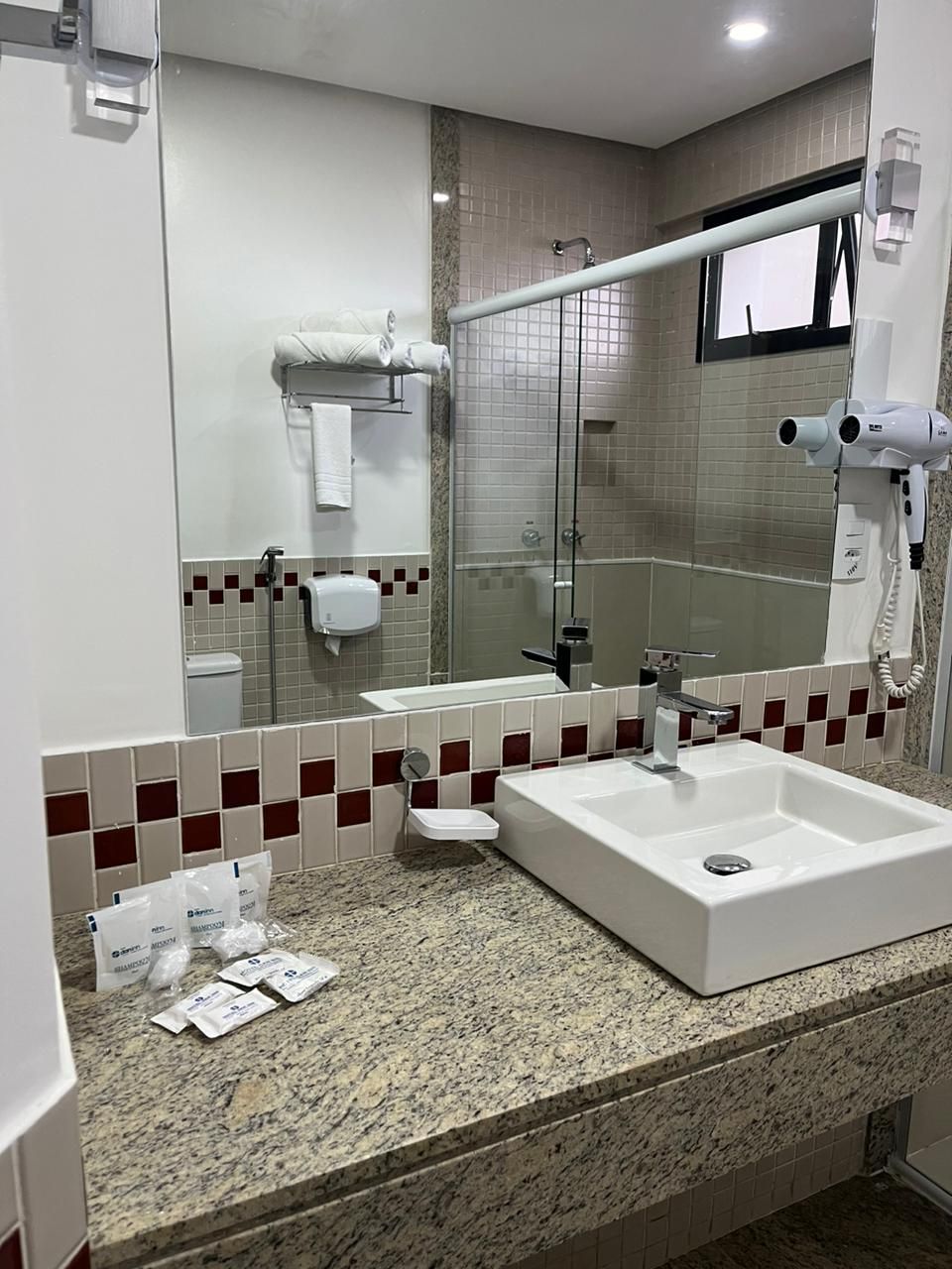 Un baño con dos lavamanos, cabina de ducha con mampara de vidrio, secador de pelo y toallero.