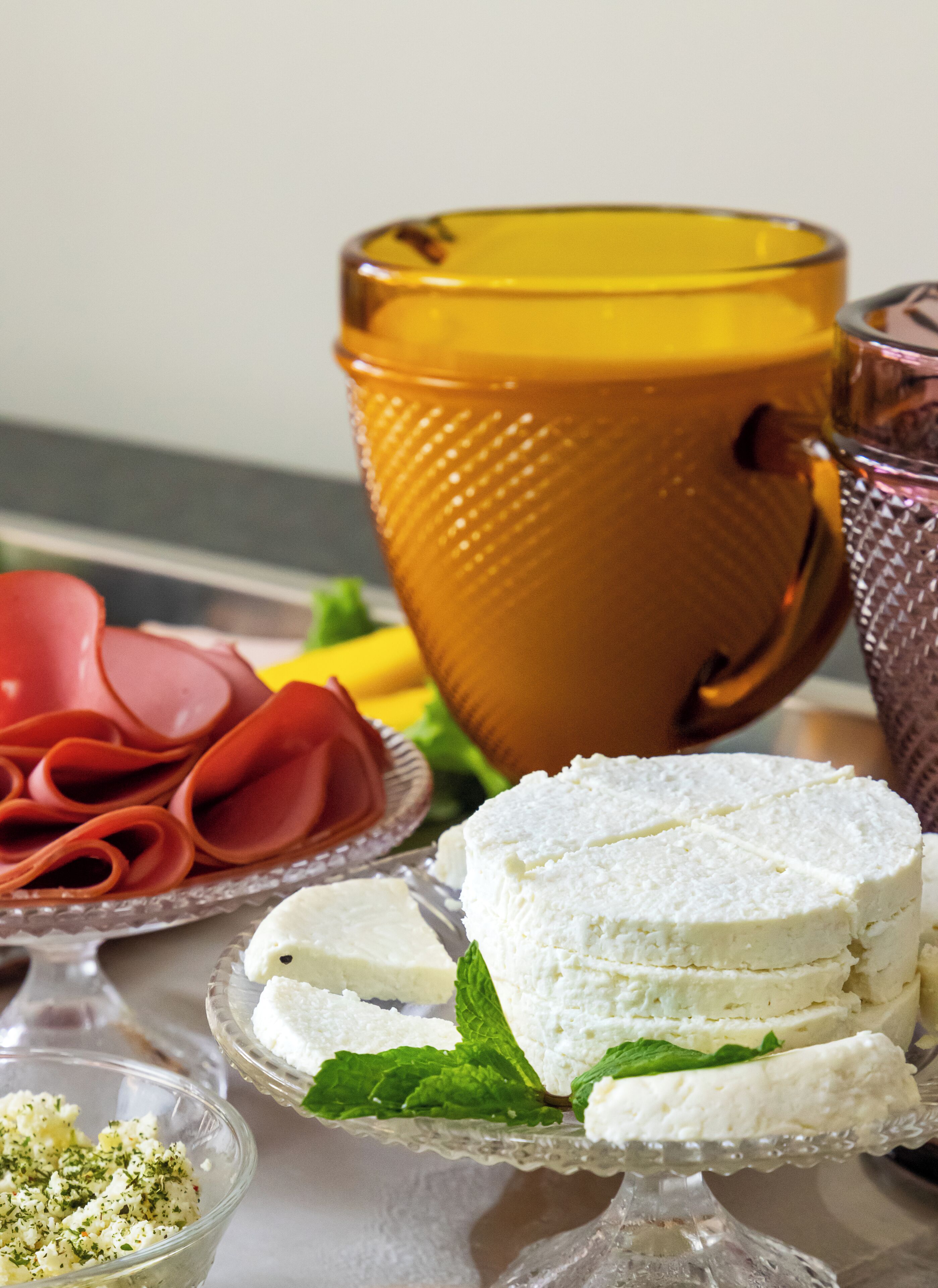 A table with various food items including cheese, ham, and a yellow cup.