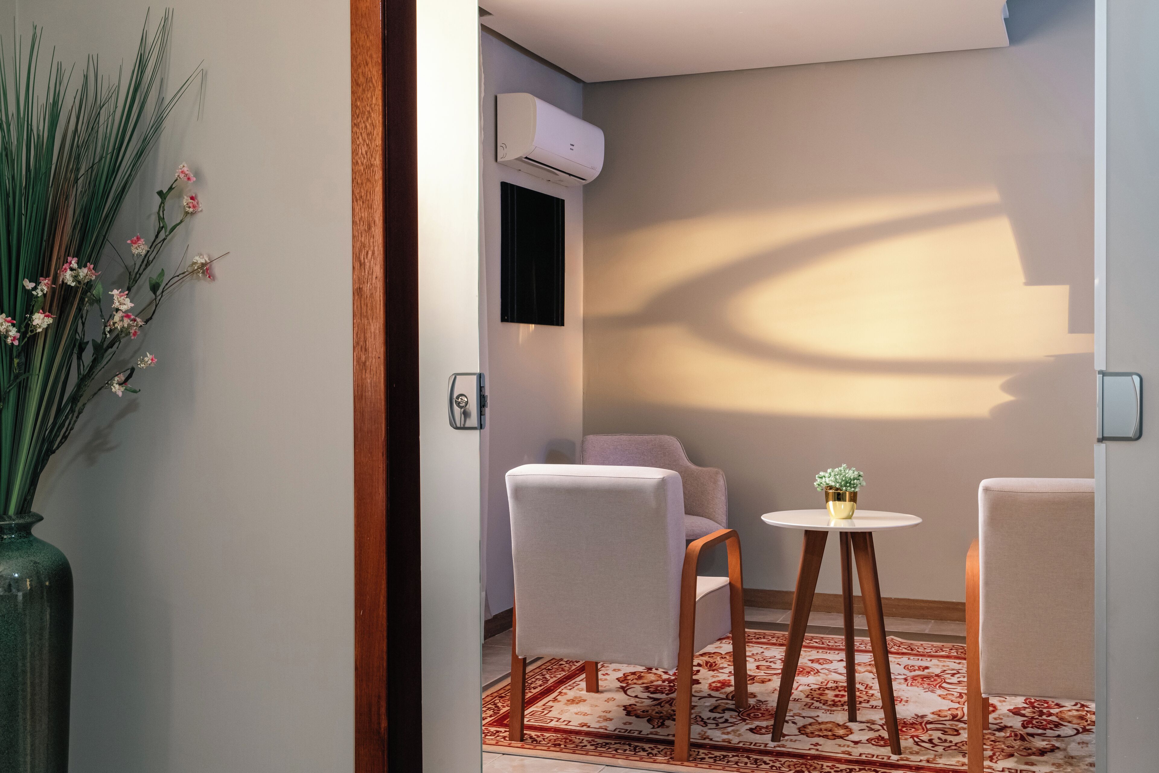 Een kamer met een bank, twee stoelen, een tafeltje met een plant, een vaas met bloemen en een airconditioning aan de muur.