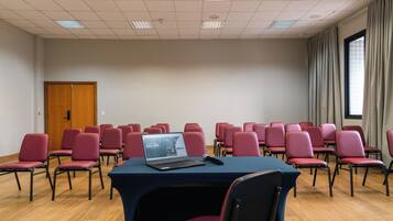 Une salle de conférence avec des rangées de chaises rouges, un ordinateur portable posé sur une table et une porte en bois.