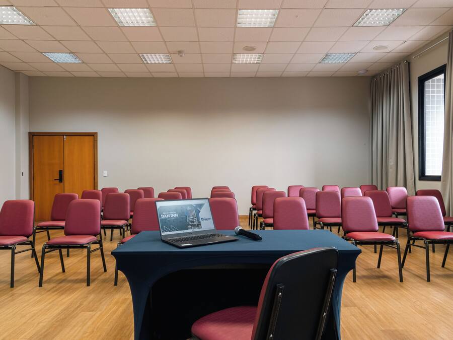Une salle de conférence avec des rangées de chaises rouges, un ordinateur portable posé sur une table et une porte en bois.