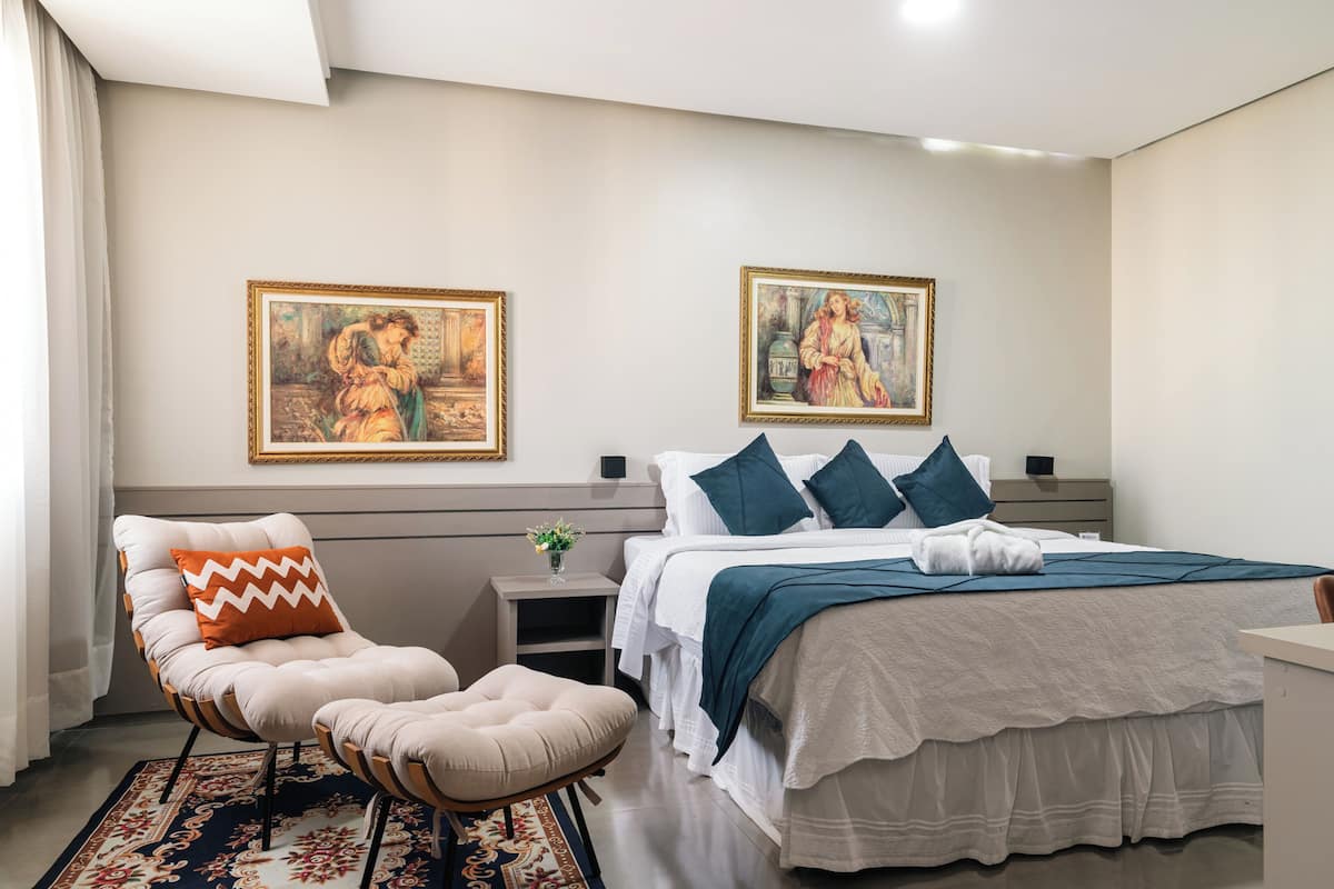 Een moderne slaapkamer met een groot bed, twee nachtkastjes, een stoel en twee ingelijste schilderijen aan de muur.
