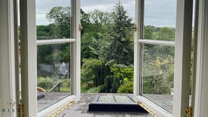 Ein offenes Fenster mit Blick auf einen üppigen Garten und eine Holzterrasse.