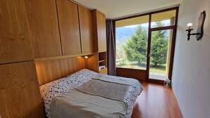 A bedroom with a bed, wooden wardrobe, and a large window with a view of greenery. - Le randonneur (Garessio)