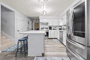 Enjoy cooking in this kitchen with a central island, bar stools, stainless steel appliances, and white cabinetry.