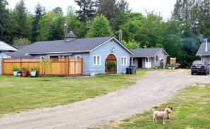 A rural road leading to a blue house with a wooden fence and potted plants. - Escape to the Creekside Hideaway (Sequim)