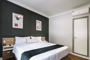 Habitación de hotel ordenada con una cama grande, mesitas de noche, un armario y dos cuadros abstractos en la pared.