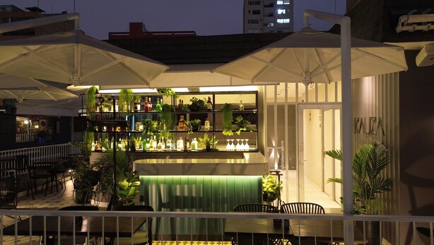 A rooftop bar with multiple levels of seating, outdoor umbrellas, and a variety of plants and bottles. - Tarata Hotel Boutique (Lima)
