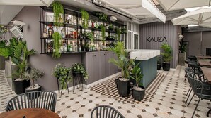 A cafe with a checkered floor, outdoor seating, and a bar area with shelves of bottles and plants. - Tarata Hotel Boutique (Lima)