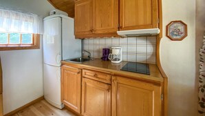 Una cocina compacta con armarios de madera, un refrigerador blanco, una cafetera y un lavamanos.