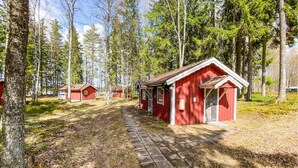 Una hilera de cabañas de madera roja con un sendero pavimentado que las conecta, rodeadas de árboles.