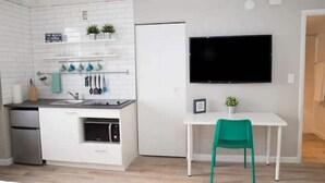 Eine moderne Küche mit weißen Schränken, einem eingebauten Ofen und einem weißen Kühlschrank. Ein weißer Esstisch mit einem grünen Stuhl und ein flachbildfernseher an der Wand.