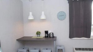 Eine kompakte Küche mit einem kleinen Tisch, zwei Hocker, einer Uhr und einem Fenster mit Vorhang.