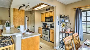 A compact kitchen with wooden cabinets, a built-in microwave, and a stove. There is a small dining area with a table and chairs.