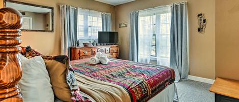 A hotel room with a large bed, a wooden headboard, a dresser with a television, and a window with curtains.