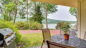 A patio with a grill, a table, and a chair, overlooking a lake and trees.