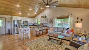 A spacious living area with a high ceiling, wooden beams, a kitchen with white cabinets, a dining area with stools, and a cozy seating area with a sofa and armchairs. - Hot Tub Relaxation & Mtn View: Sky Blue Overlook (Marble)