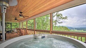 A hot tub with a wooden deck and large windows overlooking a forested landscape. - Hot Tub Relaxation & Mtn View: Sky Blue Overlook (Marble)