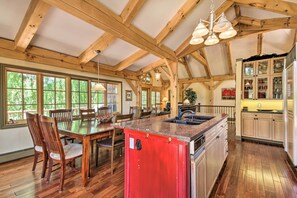 A spacious kitchen with wooden beams, a central island, and a dining area with wooden chairs.