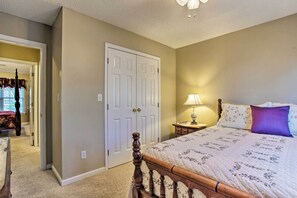 A bedroom with a wooden bed, a nightstand with a lamp, and a door leading to another room. - Asheville Area Home W/patio-11 Mi to Biltmore (Fletcher)