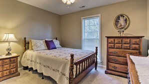 Un dormitorio con una cama de madera, una mesita de noche con lámpara, un aparador y una ventana con persianas.