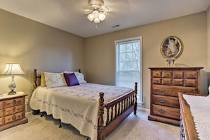 Quarto com cama de madeira, mesa de cabeceira com abajur, cômoda e janela com persianas.