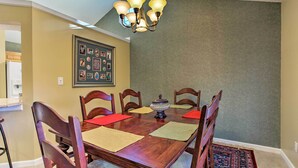 Un comedor con mesa de madera, sillas, una araña y un collage enmarcado en la pared.