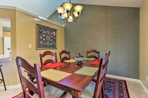 Uma sala de jantar com mesa de madeira, cadeiras, um candelabro e uma colagem emoldurada na parede.