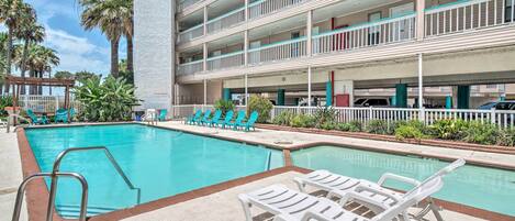 A pool area with lounge chairs and a building with multiple balconies.