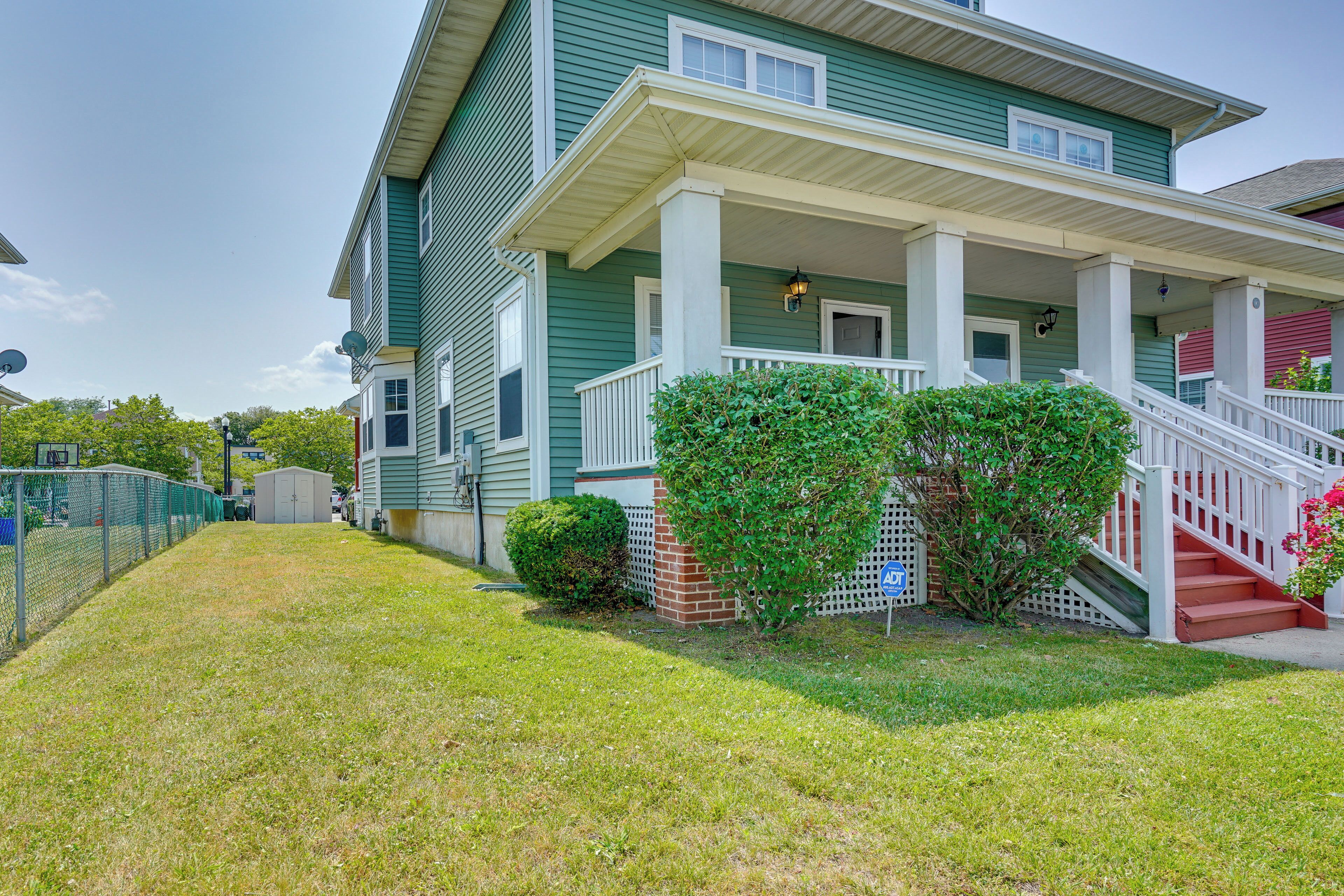 A two-story house with a front porch, a small brick structure, and a fenced yard.