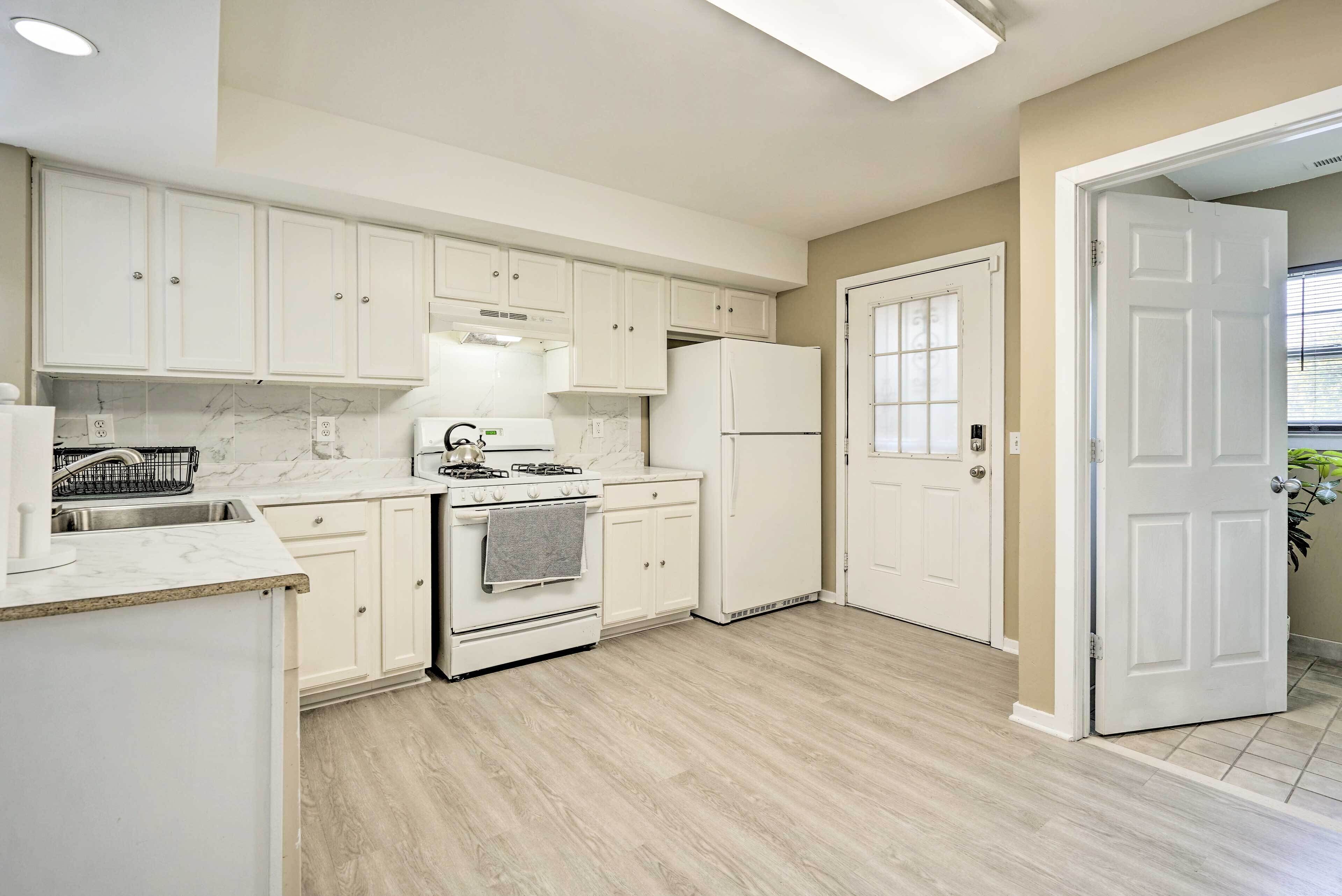 A kitchen with white cabinets, a stove, a refrigerator, and a door leading to another room.