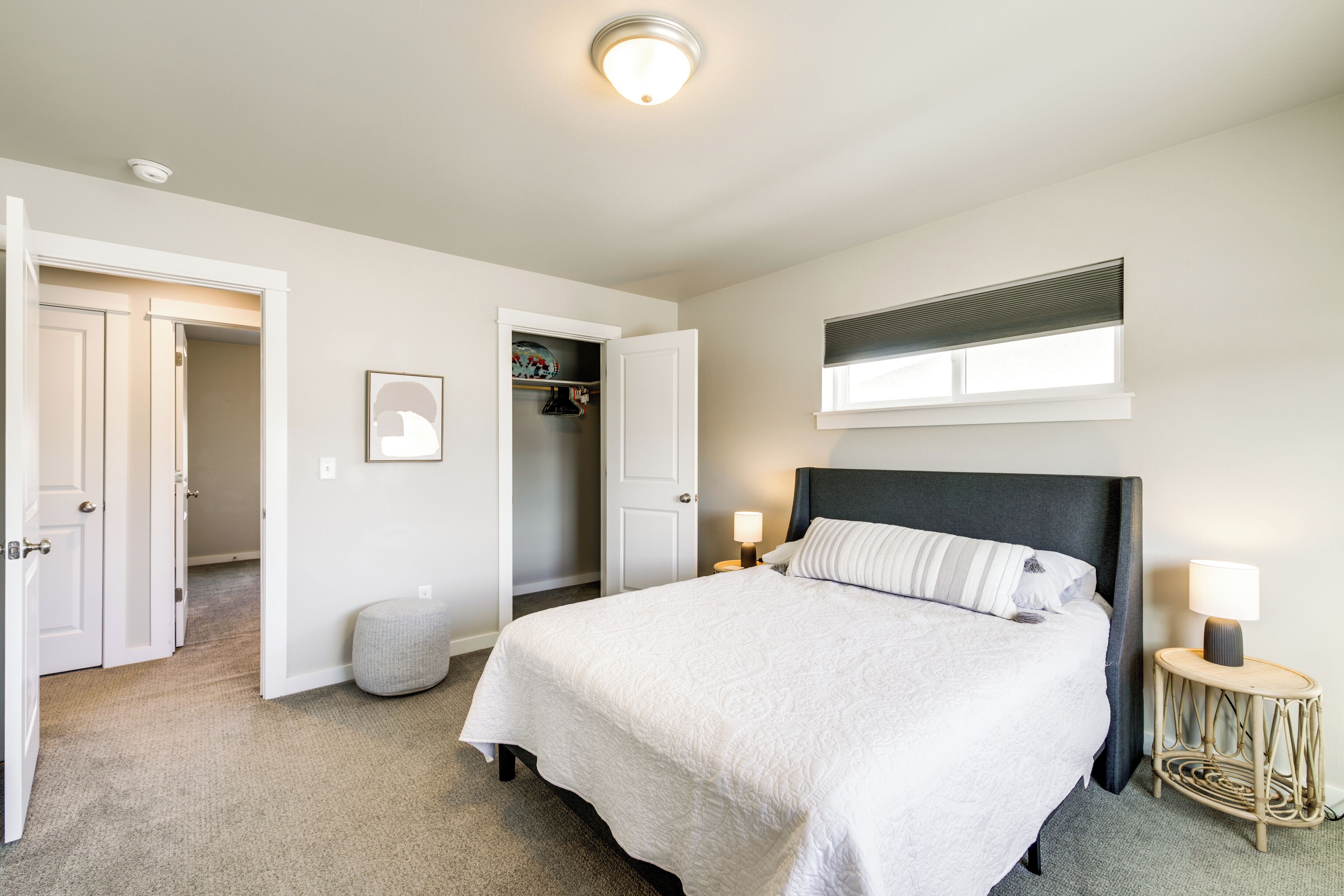 Un dormitorio con cama, lámparas de noche, una ventana, un armario y una puerta que da a otra habitación.
