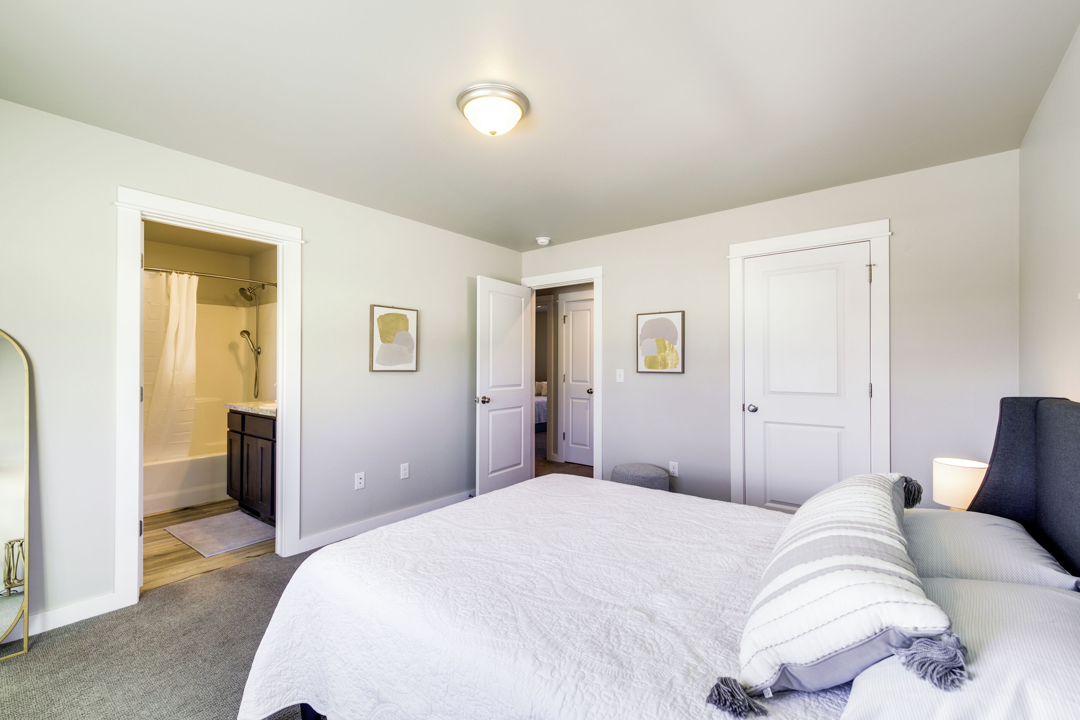 A bedroom with a bed, a bedside table, a lamp, and a door leading to a bathroom.