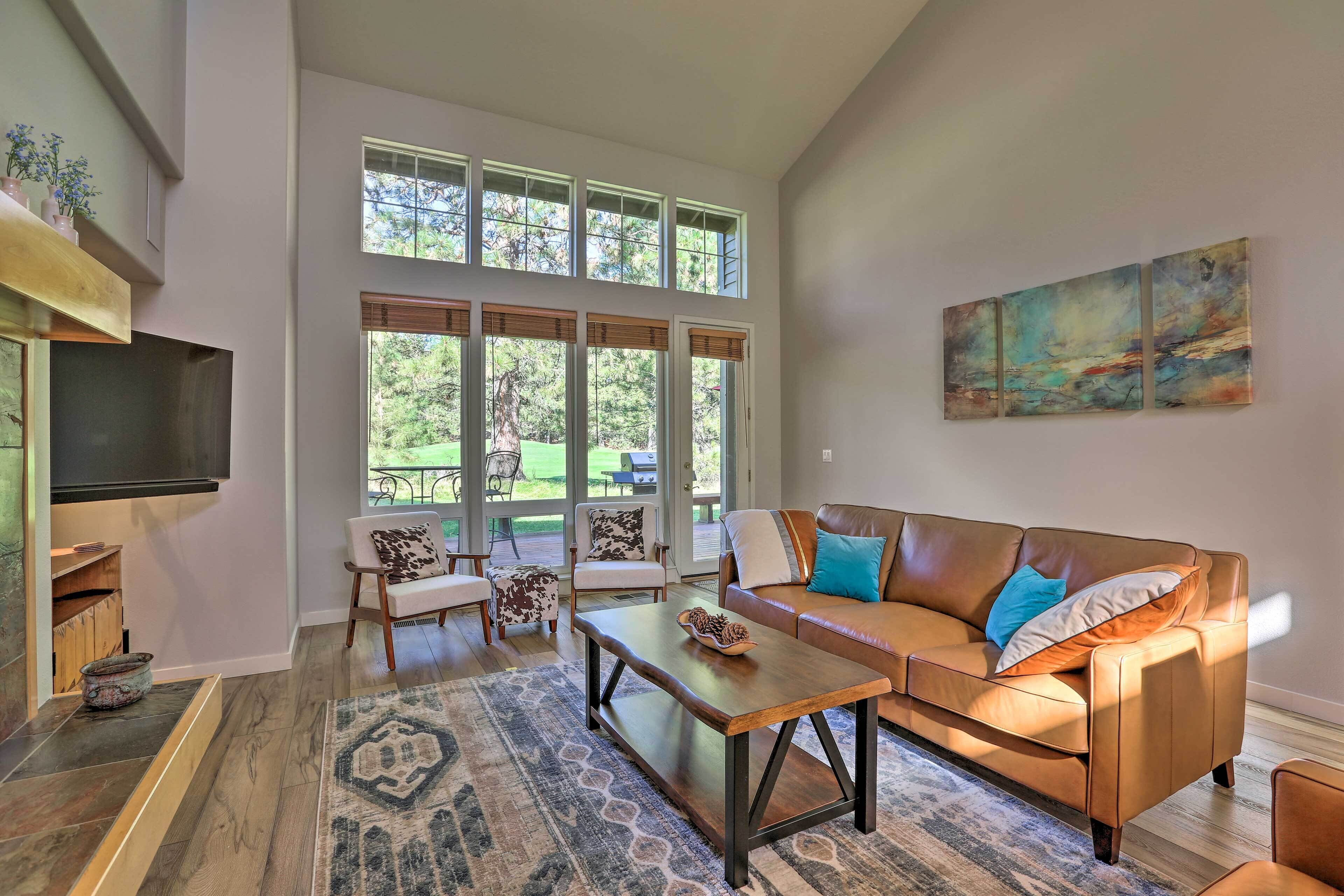 A spacious living room with a large window, a leather sofa, a coffee table, and a flat-screen TV.