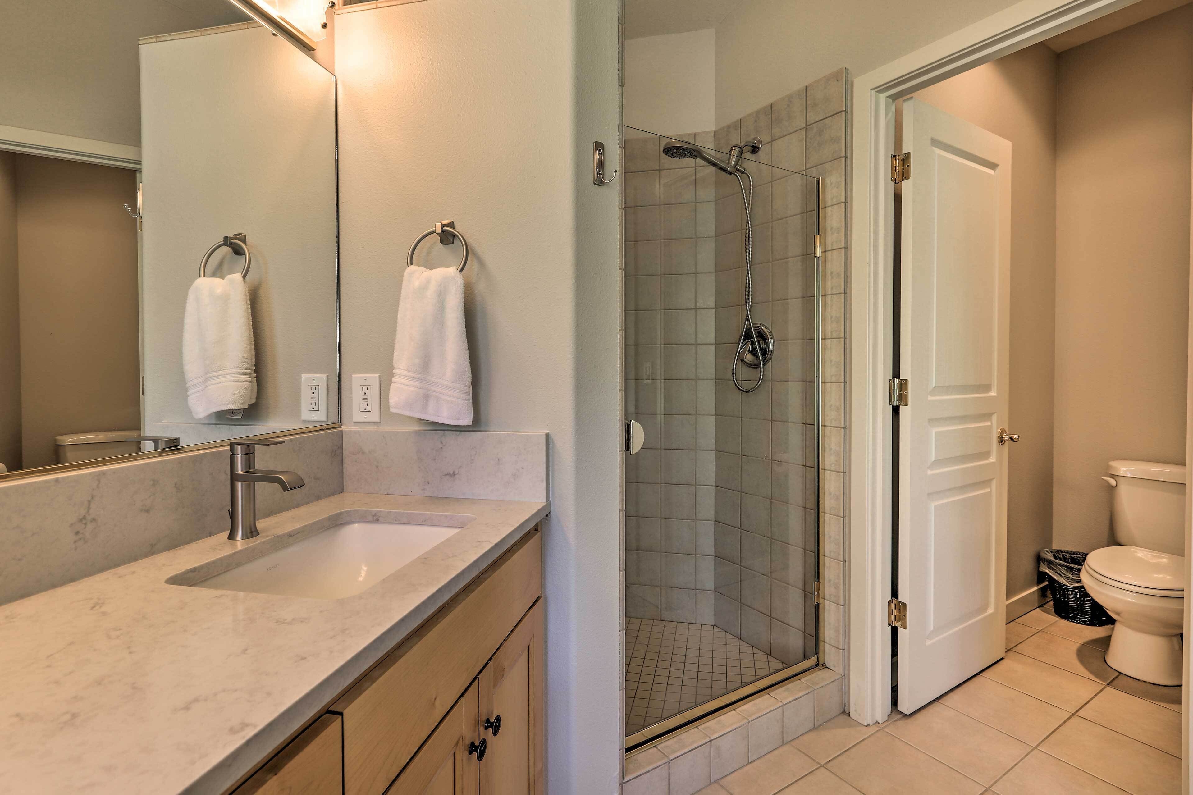 A bathroom with a sink, mirror, towel rack, shower, and toilet.