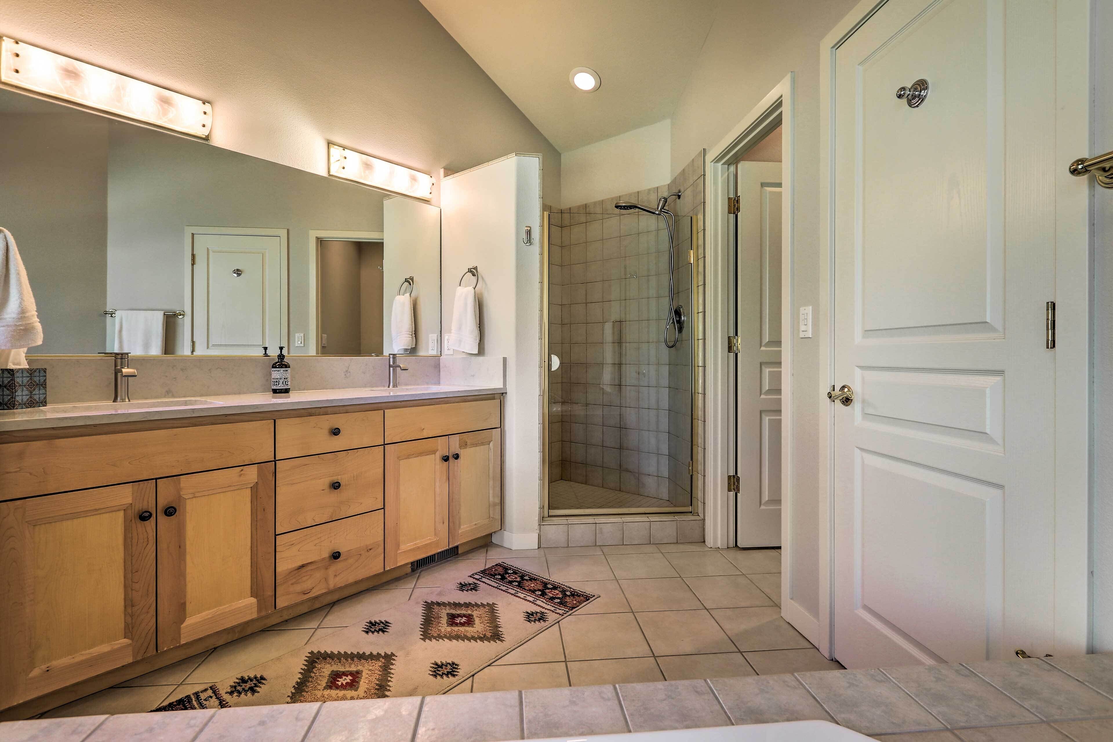 Une salle de bain avec un meuble-lavabo en bois, un grand miroir, une douche et un tapis à motifs.