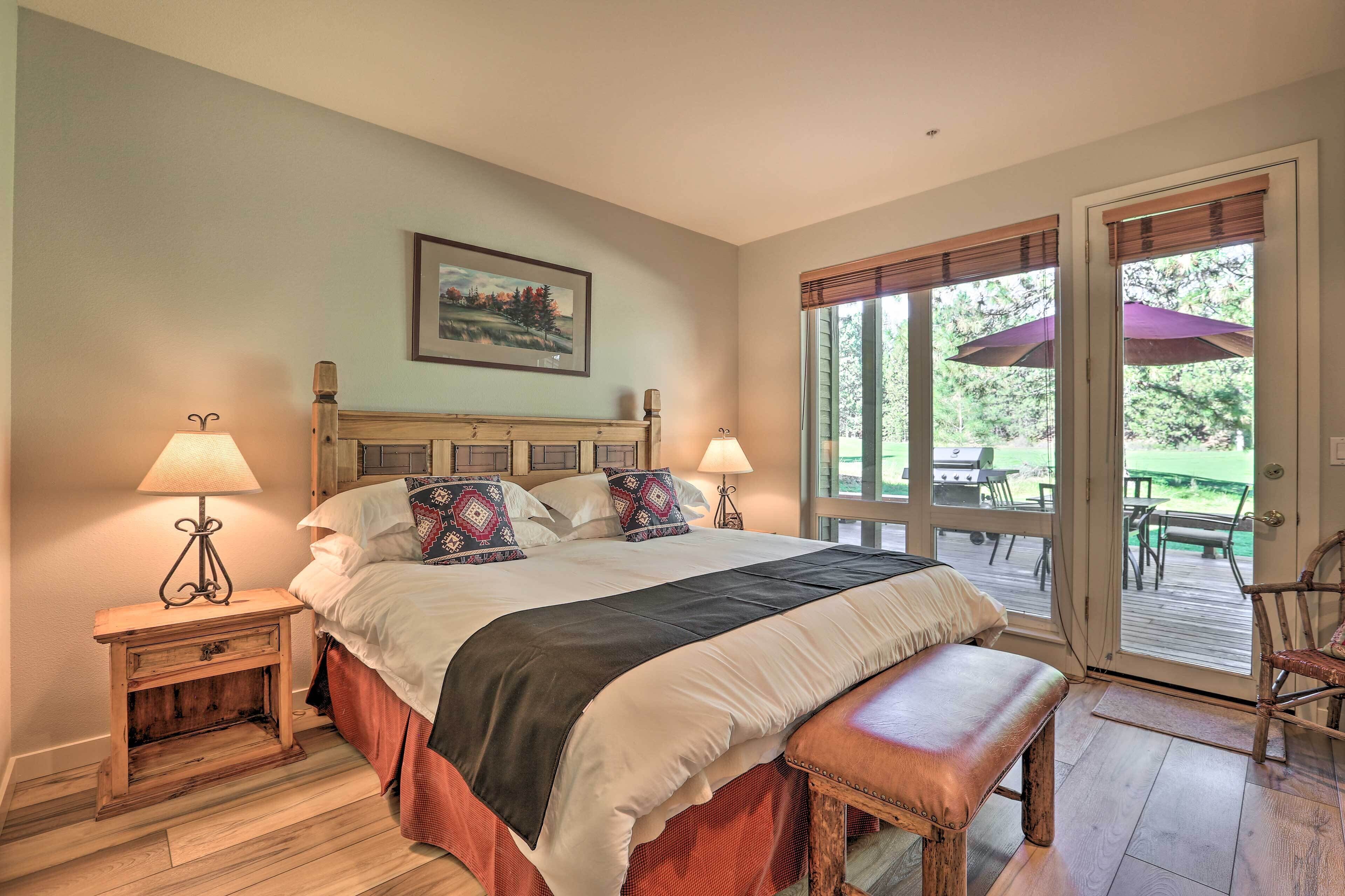 A bedroom with a large bed, two bedside tables with lamps, a bench, and a sliding glass door leading to an outdoor patio.