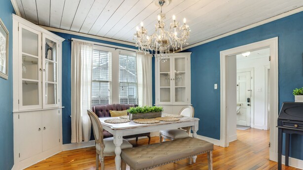 A dining area with a white table, bench, and chandelier, against a blue wall with wooden flooring. - Adorable Baton Rouge Cottage < 3 Mi to Lsu! (Baton Rouge)