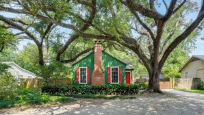 A green house with a brick chimney, surrounded by trees and a gravel driveway. - Adorable Baton Rouge Cottage < 3 Mi to Lsu! (Baton Rouge)