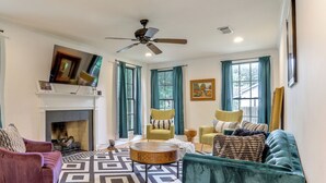 A living room with a fireplace, a ceiling fan, and a large window with curtains. - Adorable Baton Rouge Cottage < 3 Mi to Lsu! (Baton Rouge)